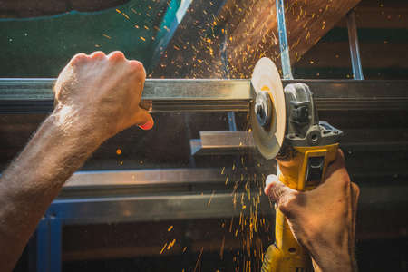 Photo of a person cutting holders, aluminium profiles or aluminium structural frames that hold drywall boards with an angle grinder in a house that is being rebuilt. Work on the roof using an angle grinderの写真素材