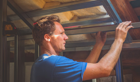 Drywall plaster wall metal fixation. A person holding and mounting aluminium drywall hangers in an attic of a house. Person using laser for making sure that everyhing is level or horizontal.の写真素材
