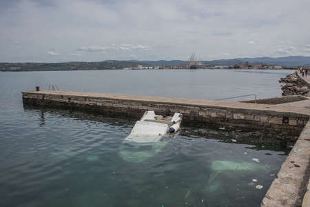 A small plastic boat partially sunk under water in a small marina close to a port of Koper in Slovenia. Debris or trash is seen floating in the water.の写真素材