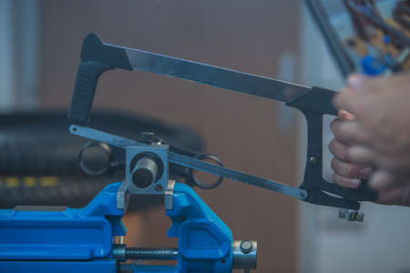 A man is holding a saw for metal and cutting through a pipe or steering tube of a bicycle while it is clamped in a vice.の写真素材