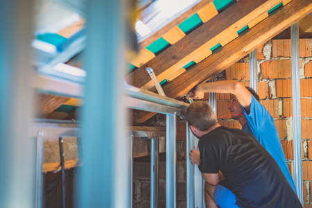 Drywall plaster wall metal fixation. A person holding and mounting aluminium drywall hangers in an attic of a house. Person using laser for making sure that everyhing is level or horizontal.の写真素材