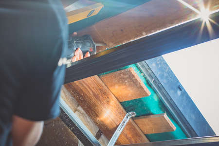 A person is cutting a board of wood next to a window with a reciprocating saw. Sawdust is flying around.の写真素材