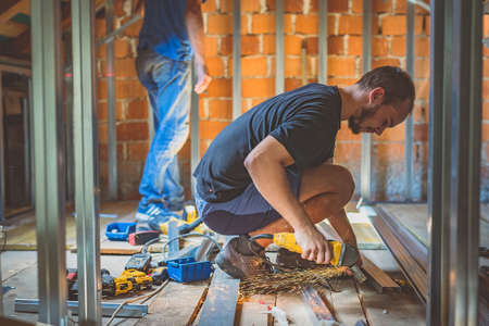 A person cutting holders, aluminium profiles or aluminium structural frames that hold drywall boards with an angle grinder in a house that is being rebuilt. Work on the roof using an angle grinderの写真素材