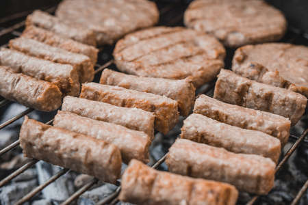 Balkan specialty - cevapcici, but made with chicken meat insted of beef or pork, which makes them recognizably lighter or whiter in color, lying on a metal grill above hot coalの写真素材