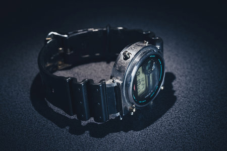 Steampunk looking digital wrist watch lying on the grainy textured table. Shiny metal wrist watch with rubber strap.の写真素材