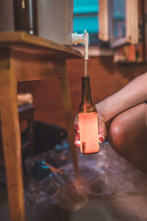 Home craft beer brewery. Final step of pouring a fresh IPA beer into a bottle from fermenter. Hand holding a bottle with glowing home made pale ale beer.の写真素材
