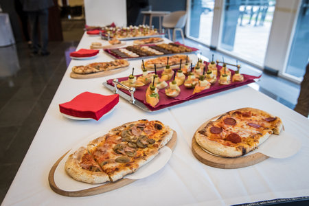 An assortiment of small pizzas, sandwiches, pastry and other food on a banquet table. Congress junk food.の写真素材