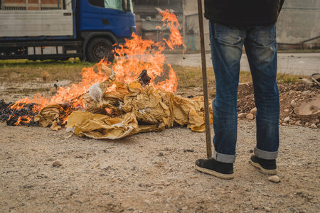 A man is burning a fire out of paper in an open space. Burning paper waste in residental or industrial environment. Pollution with burning paper.の写真素材