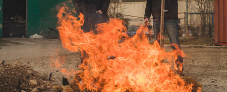 Two men burning a fire out of paper in an open space. Burning paper waste in residental or...