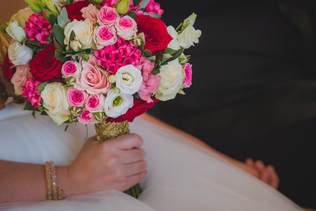 Arm of a woman holding a beautiful wedding bouquet made of red pink and white flowers, mostly roses. Other hand is seen holding a groom. Focus on the roses.の写真素材