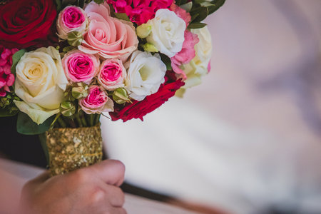 Arm of a woman holding a beautiful wedding bouquet made of red pink and white flowers, mostly roses. Other hand is seen holding a groom. Focus on the roses.の写真素材