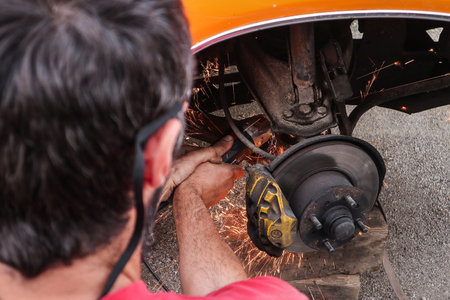 Amateur car mechanic is lowering a car with cutting the springs. Cheap lowering of a car. Angle grinder is being used on an installed spring.の写真素材