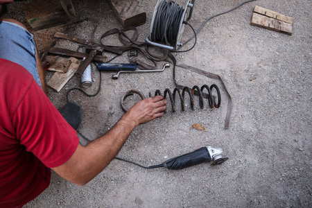Amateur car mechanic is lowering a car with cutting the springs. Cheap lowering of a car. Different tools visible on the ground.の写真素材
