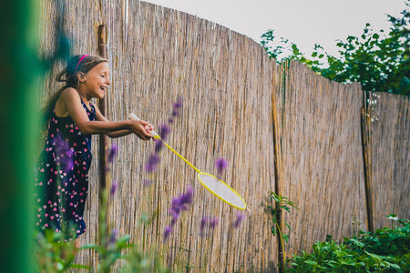 Young caucasian girl or kid is playing badminton game in a lush green garden. Kid laughing in a garden while holding a racketの写真素材