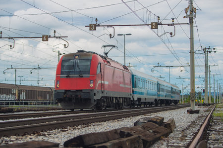 Modern electrical train  with red engine on track on a suburban station. Passenger train rushing towards the city in a suburban environment on a cloudy day.の写真素材