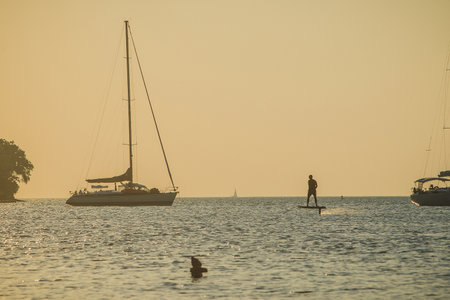 Silhuette of a man cruising on a foilboard on during a summer evening at the seaside. Riding between yachts.の写真素材
