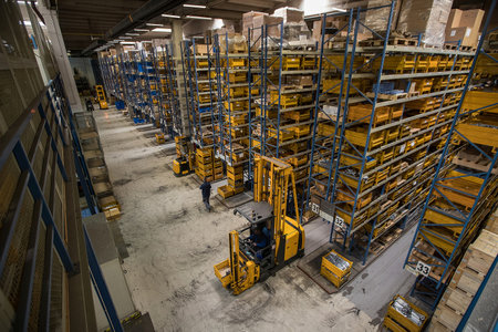 Interior of a distribution warehouse viewed from above. View onto blue storage racks and yellow boxes. Logistics and warehousing in full action with forklift and a lot of goods aroundの写真素材