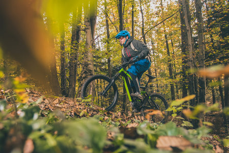 Biker riding uphill with a modern electric bicycle or mountain bike in autumn or winter setting in a forest. Modern e-cyclist in woods.の写真素材