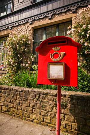 Red square mailbox in Belgium, in front of a typical house and some foliage in the background.の写真素材