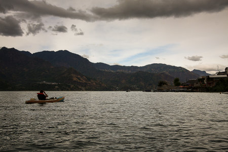 A person in a kayak, kayaking on the waters of Atitlan Lake in Guatemala. Cloudy day with mountains in the background and San Pedro village.の写真素材