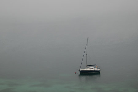 Small sailboat sitting on lake in the foggy autumn morning on a lake of Attersee in Austria.の写真素材
