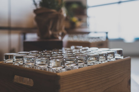 A group of glasses for juice at an event or reception stored in a fancy wooden boxes, waiting to be taken out. Focus on the glasses, green decoration between the boxes in soft focus.の写真素材