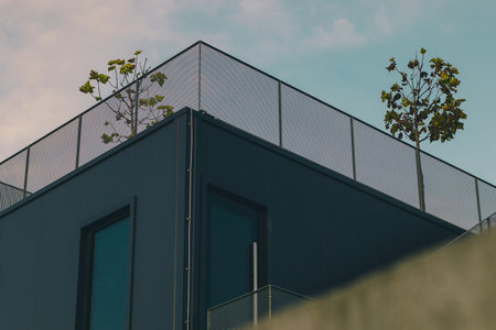 Modern facade of a house with visible metal railing and trees on top.の写真素材