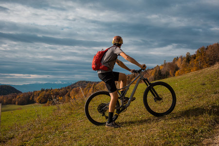 Young caucasian mountain biker resting and posing on sunny meadow in autunn setting. Visible mountains in the background.の写真素材