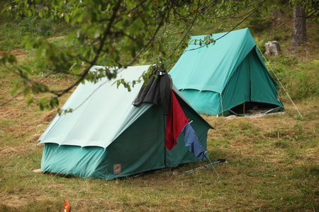 Two triangular tents in green color erected in nature. Some clothes are drying in front of one.の写真素材
