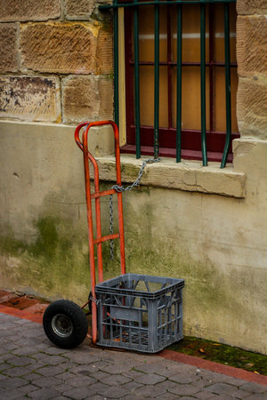 A red hand trolley with an empty gray box is chained to a metal railing on the window. Funny thing.の写真素材