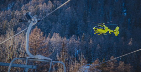 A yellow rescue helicopter is taking of in the middle of the ski slope area in a big cloud of snow. Concept of helicopter rescue on snow or ski slope. Visible ski lift.の写真素材