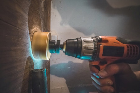 A man using a battery powered drill with a circular saw bit to drill a hole in a wooden plank. Vacuum cleaner is visible to suck the excess dust away.の写真素材