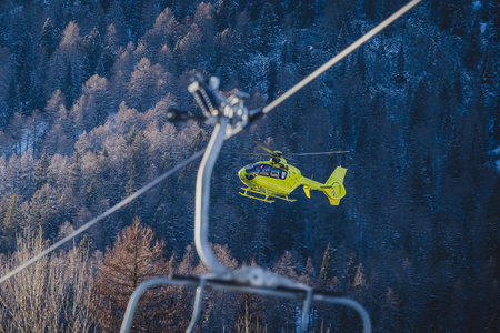 A yellow rescue helicopter is taking of in the middle of the ski slope area in a big cloud of snow. Concept of helicopter rescue on snow or ski slope. Visible ski lift.の写真素材