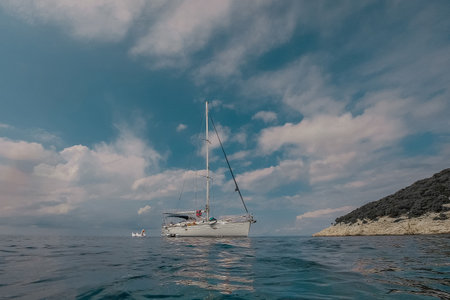 Low profile of a modern sailboat or yacht moored in a beautiful lagoon in adriatic. White sailboat with sails stowed floating in the summer seaの写真素材
