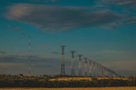 A row of pylons for power lines through a field in Ukraine. Next to it there is a radio tower...