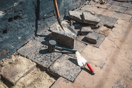 View of construction works on a sidewalk . tile or granite blocks on a pedestrian path on a street. Visible open floor with hammer, sand and other tools aroundの写真素材