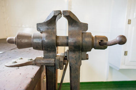 An old metal vice clamp used to hold things steadily, mounted in an old workshop bench with green floorの写真素材