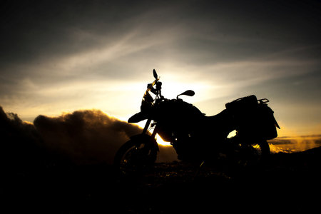 Silhouette of an adventure motorcycle on the top of the mountain with some clouds rising above.の写真素材