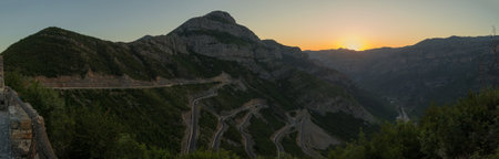 Panorama of epic roads in the north albanian mountains, famous curves and hairpin turns of SH20 road above the Cem river gorge at sunset. Sun is just setting behind the mountains.の写真素材