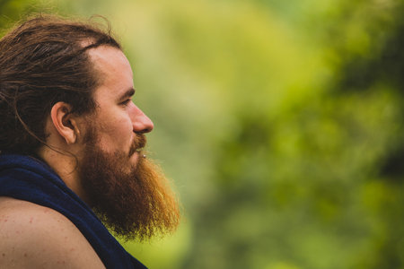 Side portrait of a hipster looking man with a long beard and hair, looking forward in the distance. Background in smooth bokeh out of focus, with plenty of copyspace.の写真素材
