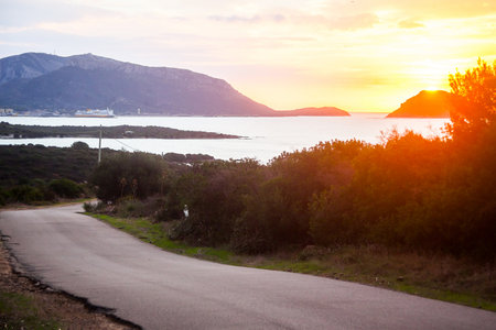 Early morning view of Golfo Aranci on Sardinia, looking towards the ferry port with a ferry visible. Asphalt road in the foreground, sun is about to rise.の写真素材