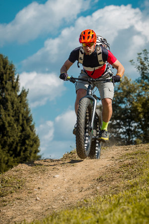 Man on a fat bike storming or riding downhill. Professional biker on a trail with a fat bike.の写真素材