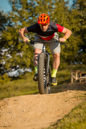 Man on a fat bike storming or riding downhill. Professional biker on a trail with a fat bike.の写真素材