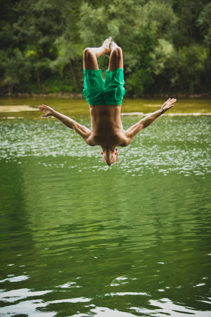 A man with green swimming shorts making a backflip into a green river with his arms wide spread.の写真素材
