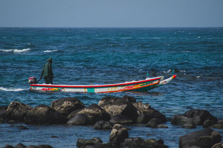 Typical fishing boat in Almadies, Dakar, Senegal, called pirogue or piragua or piraga with a fisherman driving the boat into a bay on a clear sunny day.の写真素材
