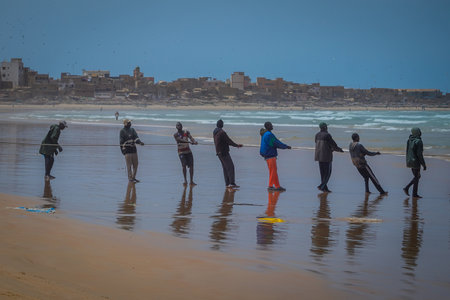 DAKAR, SENEGAL, FEBRUARY 18 2017:  A row of local fishermen pulling the rope with fishing net out of the water on the picturesque beach of Yoff in Senegal, Africa.のeditorial素材