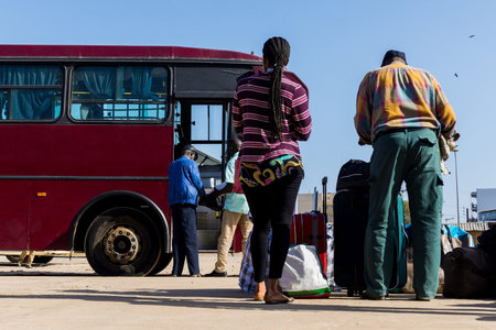People waiting with luggage to embark on a bus from Dakar to Ziguinchor in Senegal, Africa. Travek with bus in Africa, people standing on a platform in front of a bus.の写真素材