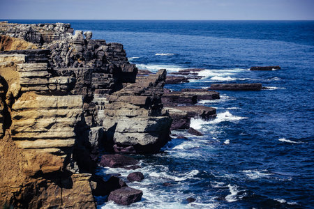 rock formations extending into the sea around Peniche, Portugal. Coastline collapse, stones in the sea, on an overcast dayの写真素材