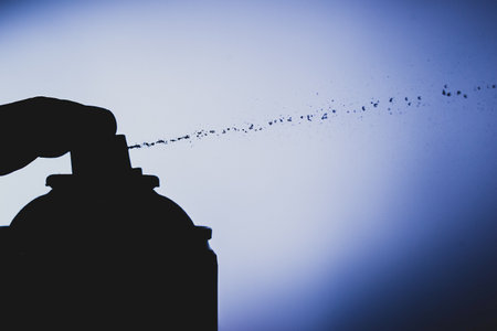 Silhouette of a spray can with drops coming out from the nozzle. Finger on the nozzle.の写真素材