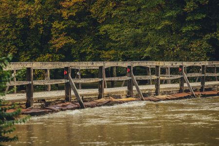 Flooded wooden trestle bridge with road, due to heavy rain and bad weather. Dirty river water flowing just over the top of the wood bridge. Dangerous rising water in flood.の写真素材
